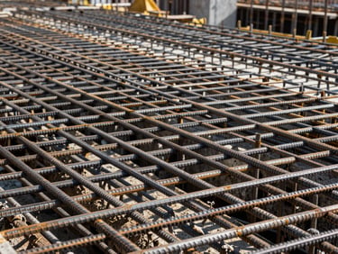 Close-up of a dense rebar grid on a construction site, steel reinforcement bars intersecting at precise intervals, concrete formwork panels visible in the background, natural daylight from above casting sharp shadows across the structural lattice, no workers, no signage