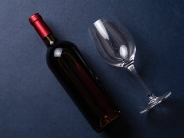 Overhead flat-lay of a dark red wine bottle and a wine glass, soft natural light, minimalist setting.