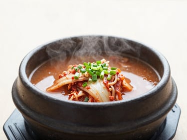 A steaming bowl of low-glycemic kimchi jjigae in a black clay pot, bright overcast natural daylight, clean editorial food photography, 35mm