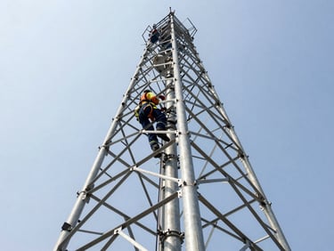 Close-up of a tower technician in PPE, actively rigging equipment on a cell tower, bright high-contrast daylight, steel and sky tones, industrial editorial photography, wide-angle architectural framing