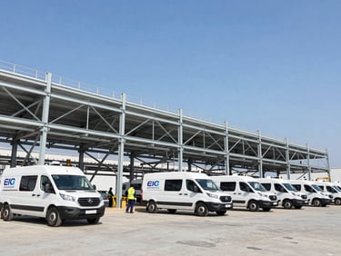 Wide environmental shot of branded EIG Wireless fleet vehicles on-site at a small cell installation, technicians visible in PPE, crisp daylight, high-contrast steel and sky tones, industrial editorial photography, wide-angle architectural framing