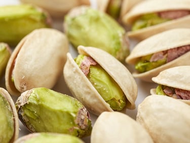 Macro shot of green peeled pistachio kernels showing intense green color grading, bright clean lighting, sharp focus.