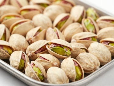 Macro close-up of graded in-shell Fandoghi pistachios on a clean steel tray, bright industrial lighting, sharp focus.