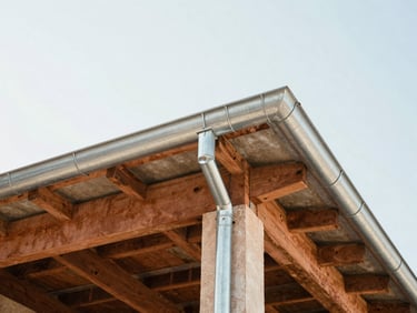 Low-angle shot looking up at a roofline showing exposed structural beams and new zinc gutters, bright daylight, 35mm