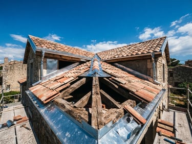 Wide shot looking up at a partially renovated terracotta roof against a bright Mediterranean sky, exposed wooden beams and new zinc flashing, rugged documentary photography, 35mm