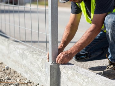 Close-up of a Carjen Fence Co. crew member carefully setting a fence post into concrete, wearing safety gear, bright daylight, focused action, 35mm lens.
