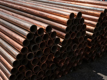 Close-up of thick copper cables and sorted pipes stacked in an industrial warehouse, high-contrast metallic textures, deep shadows