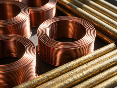 Close-up of bright copper wire coils and sorted brass pipes, metallic textures, high contrast, deep shadows
