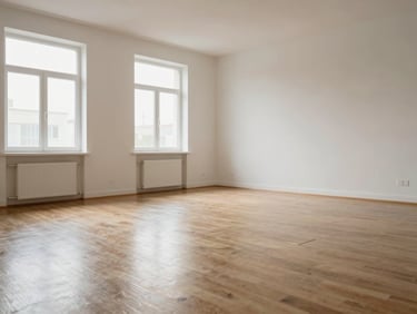 Wide environmental shot of an empty apartment living room after cleaning — bare floors polished to a shine, windowsills dust-free, walls clean, soft diffuse daylight filling the space, no furniture or occupants