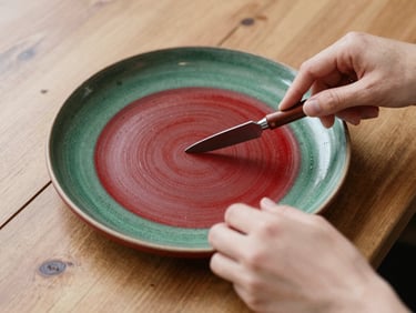 Overhead 35mm photograph of hands styling a rustic plate on a wooden table, soft natural side-light, rich crimson accents.