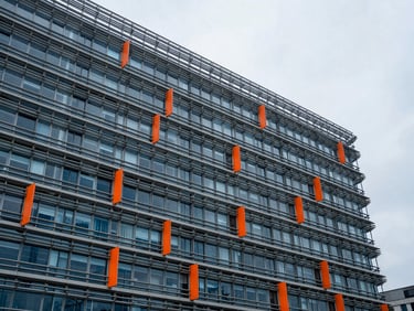 Cool editorial architectural detail of the European Commission building in Brussels, diffused overcast daylight, muted corporate blues, sharp orange safety accents, 35mm lens