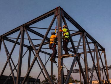 Primer plano de un técnico inspeccionando una estructura de truss de escenario robusta, con arneses de seguridad y fondo de un cielo despejado.