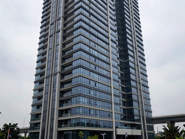 Architectural exterior of a luxury high-rise residential tower on Dwarka Expressway, glass curtain-wall facade, overcast daylight, low vantage point looking upward along the building edge, expressway infrastructure visible in the background