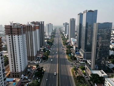 Aerial drone view of Dwarka Expressway corridor in Gurgaon at midday—multi-lane expressway stretching toward the horizon, flanked by high-rise residential towers under construction and completed glass towers, overcast soft light, no people, wide environmental framing showing strategic corridor position