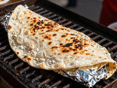 Close-up of a giant flour tortilla wrapped tight and seared on the grill, foil wrapping peeled back.