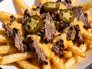 Close-up of golden street fries loaded with chopped grilled steak, melted cheese, and fresh jalapeños, high-contrast daylight.