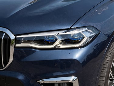 High-contrast shot of a dark blue BMW X7 headlight and grille, sharp metallic reflections.