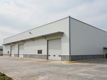 Environmental shot of a single-story light industrial warehouse building exterior, flat roof, roll-up doors visible along facade, overcast daylight, concrete apron in foreground, no people, wide documentary frame