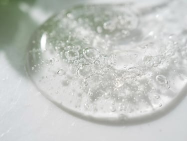Macro shot of a clear viscous serum texture with tiny air bubbles on a clean white laboratory surface, soft green shadows, clinical daylight, 35mm