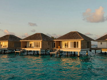 Wide environmental landscape of a private overwater villa in the Maldives at golden hour, turquoise water, warm cinematic light, 35mm lens.