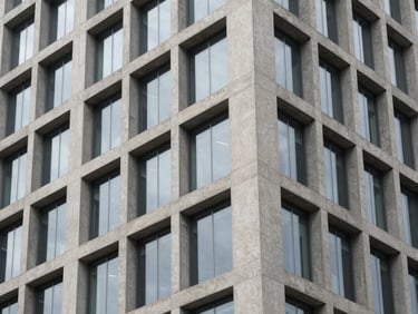 Minimalist architectural detail of a modern concrete high-rise facade with glass panels reflecting soft overcast daylight, clean geometric lines.