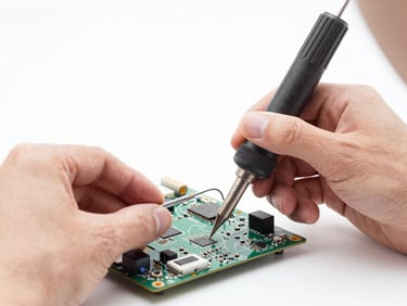 Close-up of a professional technician's hands using micro-soldering tools on a laptop motherboard under bright studio lights, clean laboratory background.