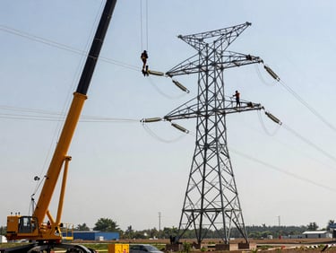 Close-up of high-voltage transmission towers being erected by crane in open terrain, steel lattice arms extended, linemen working aloft, clear sky, wide site visible in background