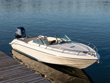 A pristine motorboat resting at a quiet private wooden dock on calm blue lake water, warm golden-hour light, wide environmental shot.