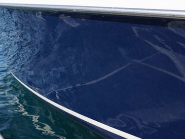 Close-up of water-beading on a highly reflective polished navy blue boat hull, bright direct sunlight, high-contrast fiberglass finish.