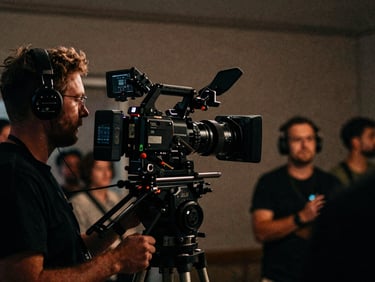 Behind-the-scenes anamorphic shot of a camera operator filming an event, low-key lighting, 35mm grain.