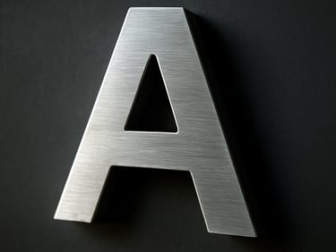 Close-up of a brushed aluminium 3D sign letter mounted on a dark wall, cool daylight raking across the raised surface revealing depth and edge detail