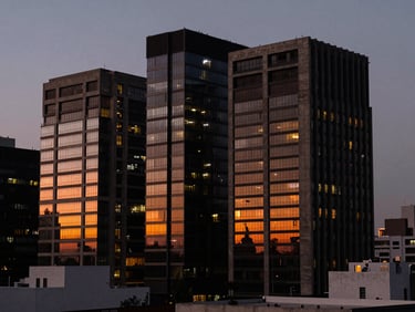 Moody architectural detail of San Pedro Garza García skyline at dusk, sharp concrete and glass structures, low-key lighting with warm orange glows reflecting in the windows, 35mm