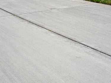Close-up of weathered residential driveway concrete, half cleaned to bare pale grey under overcast natural light, grime line visible across centre