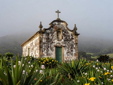 Fachada de uma antiga casa de pedra basáltica cercada por vegetação verdejante e flores sob a névoa da serra ao amanhecer.