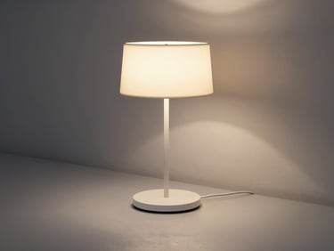 A minimalist designer table lamp casting warm, diffused ambient light on a silver-gray surface.