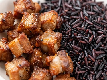 Close-up macro shot of crisp golden-brown griot pork chunks next to fragrant black djon djon rice, warm natural lighting.