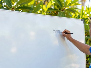 Hands writing on a large whiteboard during an outdoor community planning session, vibrant green foliage in background, bright Florida sunlight, 35mm
