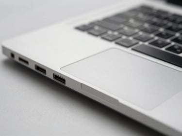 Close-up straight-on shot of a laptop port array — USB-C, HDMI, and SD slots visible on the aluminium edge, neutral overcast-day lighting, sharp detail, no hands, no background clutter