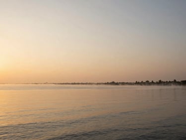 Serene coastal view of Chilika Lake at sunrise, with calm waters reflecting the sky, soft morning mist, wide-angle lens, warm editorial travel photography.