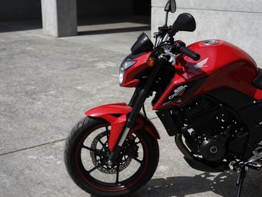 Close-up of a red Honda CB 250 Twister parked in a modern concrete courtyard, sharp automotive photography, high-contrast lighting, deep shadows, crisp details, 50mm lens