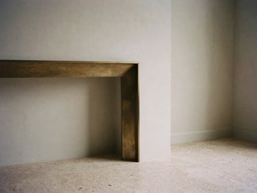Detail shot of a minimalist living room corner, showing brushed bronze fireplace trim meeting seamless travertine flooring, soft afternoon directional light, medium format film.