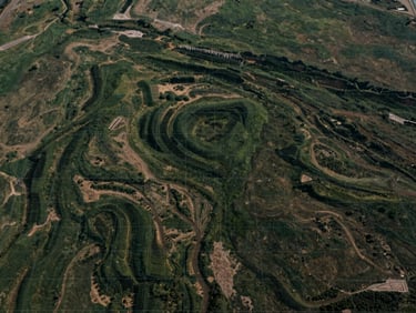 Wide shot of undeveloped land with clear topography and faint grid lines overlaid, under soft overcast daylight, muted earth tones and deep greens, high-end real estate