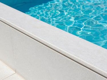 Close-up architectural detail of smooth remarblelite pool plaster texture under bright midday sun, clean coping stone edge, sharp focus.