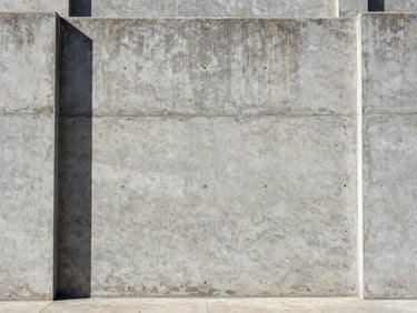 Symmetrical straight-on architectural shot of a massive concrete foundation wall, harsh natural sunlight casting sharp shadows, desaturated industrial tones, sharp focus.