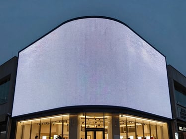 Dusk shot of a flagship retail facade with a massive weatherproof LED display, high-contrast architectural lighting.