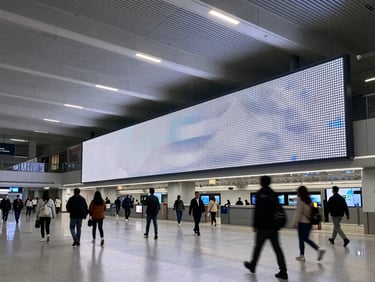 Wide architectural shot of a transit hub terminal with integrated high-luminosity LED displays, passengers in motion blur.