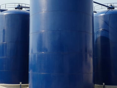 Industrial GRP storage tanks, cylindrical blue composite structures, high-contrast factory daylight, 35mm