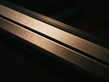 Abstract macro shot of premium brushed steel and matte black glass, sharp side-lighting, warm amber highlights, 35mm film