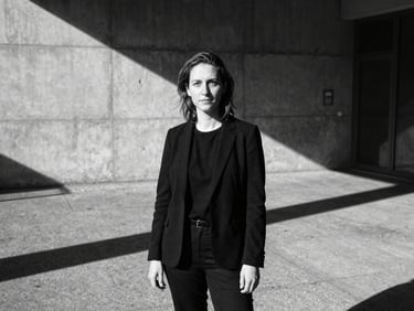 High-contrast black-and-white portrait of a female curator in Berlin, hard direct sunlight casting dramatic shadows, sharp focus, industrial concrete background.