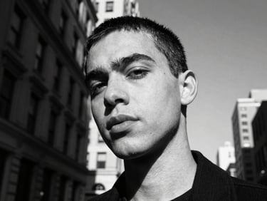 High-contrast black-and-white close-up portrait of a non-binary creator in New York, dynamic Dutch perspective, hard direct sunlight, deep shadows.